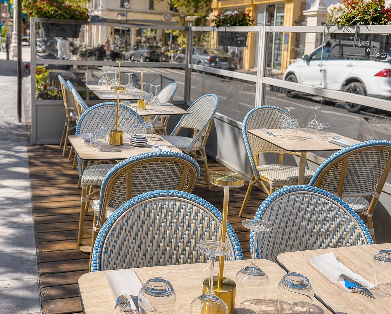 Terrasse de MIKI à Nice, tables en bois clair et chaises de rotin bleu et blanc, lumière du sud
